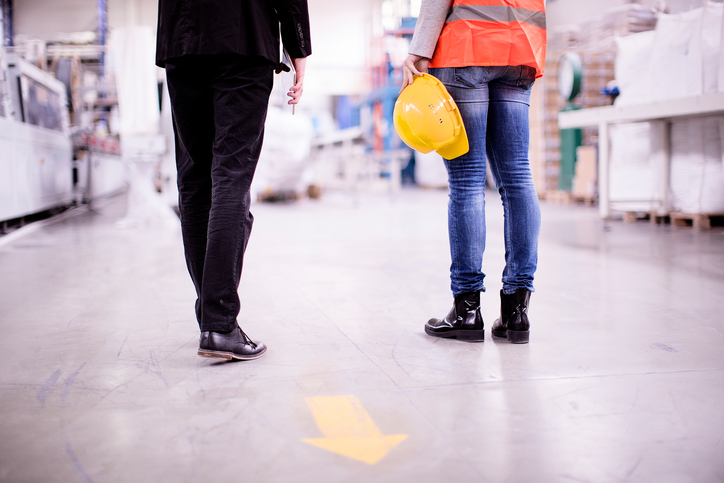 A worker holds a hard hat while standing with her supervisor to discuss safety training