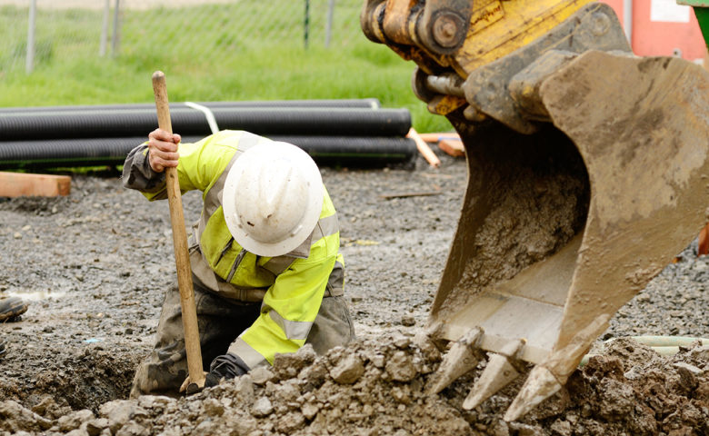 Construction worker digging dirt in trench with the help of a digger