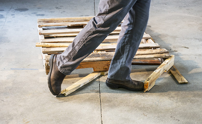 Man tripping over a damaged pallet with nails sticking out of it