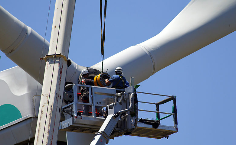 Men fully dressed in PPE repairing wind turbine