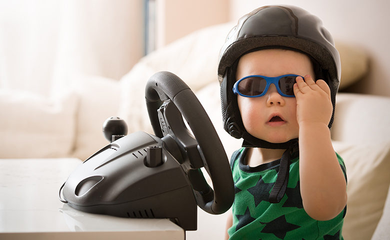 Funny picture of a baby behind the wheel with a helmet and sunglasses on.