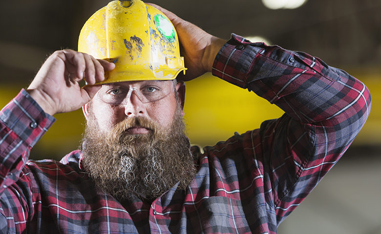 Bearded construction worker putting on hardhat