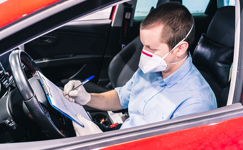 A technician doing a security inspection inside a vehicle protected with a mask and gloves to prevent the spread of virus