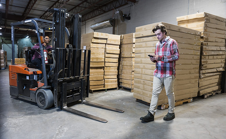 An accident waiting to happen. An industrial worker using a cell phone in a warehouse.