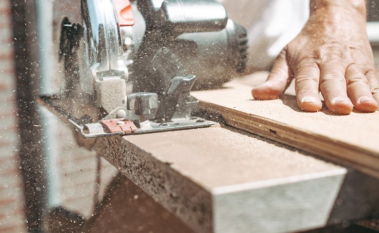 Carpenter using circular power saw for cutting wood, home improvement, do it yourself (DIY) and construction works concept, action shot