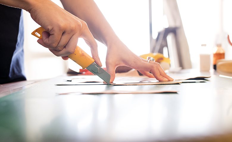 Young woman artisan cutting leather with a utility knife