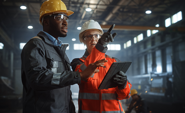 Two Heavy Industry Engineers Stand in Steel Metal Manufacturing Factory, Use Digital Tablet Computer and Have a Discussion. Black African American Industrial Specialist Talk to Female Technician.