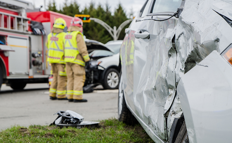 Close up on a car crashed with fireman in background