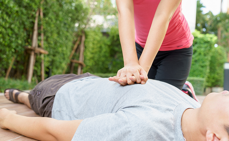 Woman giving cardiopulmonary resuscitation (CPR) to a man at public park.