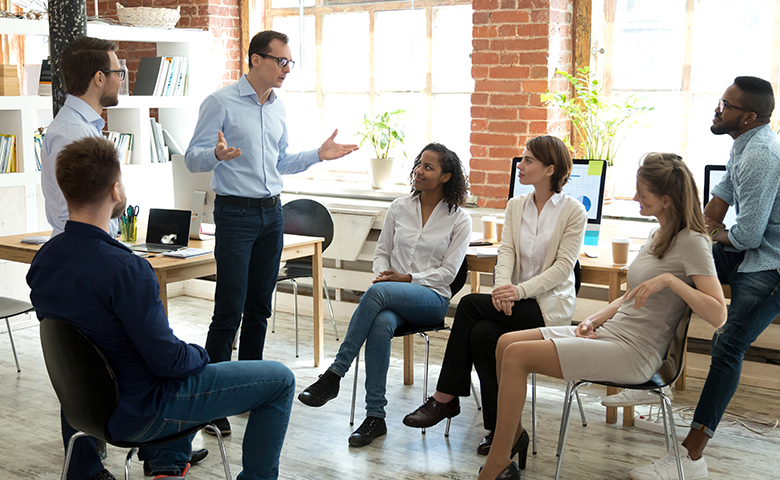 Diverse employees listening to male manager speaking at group meeting